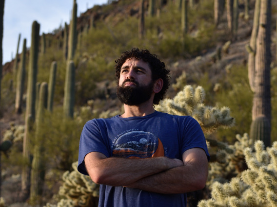 Curly haired man crossing arms looking into the distance in a desert landscape. 